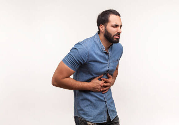 Unhappy depressed man with beard holding hands on stomach feeling acute pain, suffering indigestion and nausea, duodenal ulcer. Indoor studio shot isolated on white background