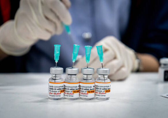 vaccine doses being prepared by gloved medical worker with syringe