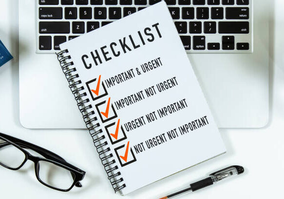 Checklist on notepad with laptop on office desk. Important and Urgent, Important Not Urgent, Urgent Not Important, Not Urgent Not Important.