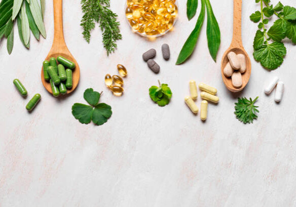 Natural vitamins, plant based supplements and green leaves on white wooden background, top view, copy space. Various organic capsules and pills.